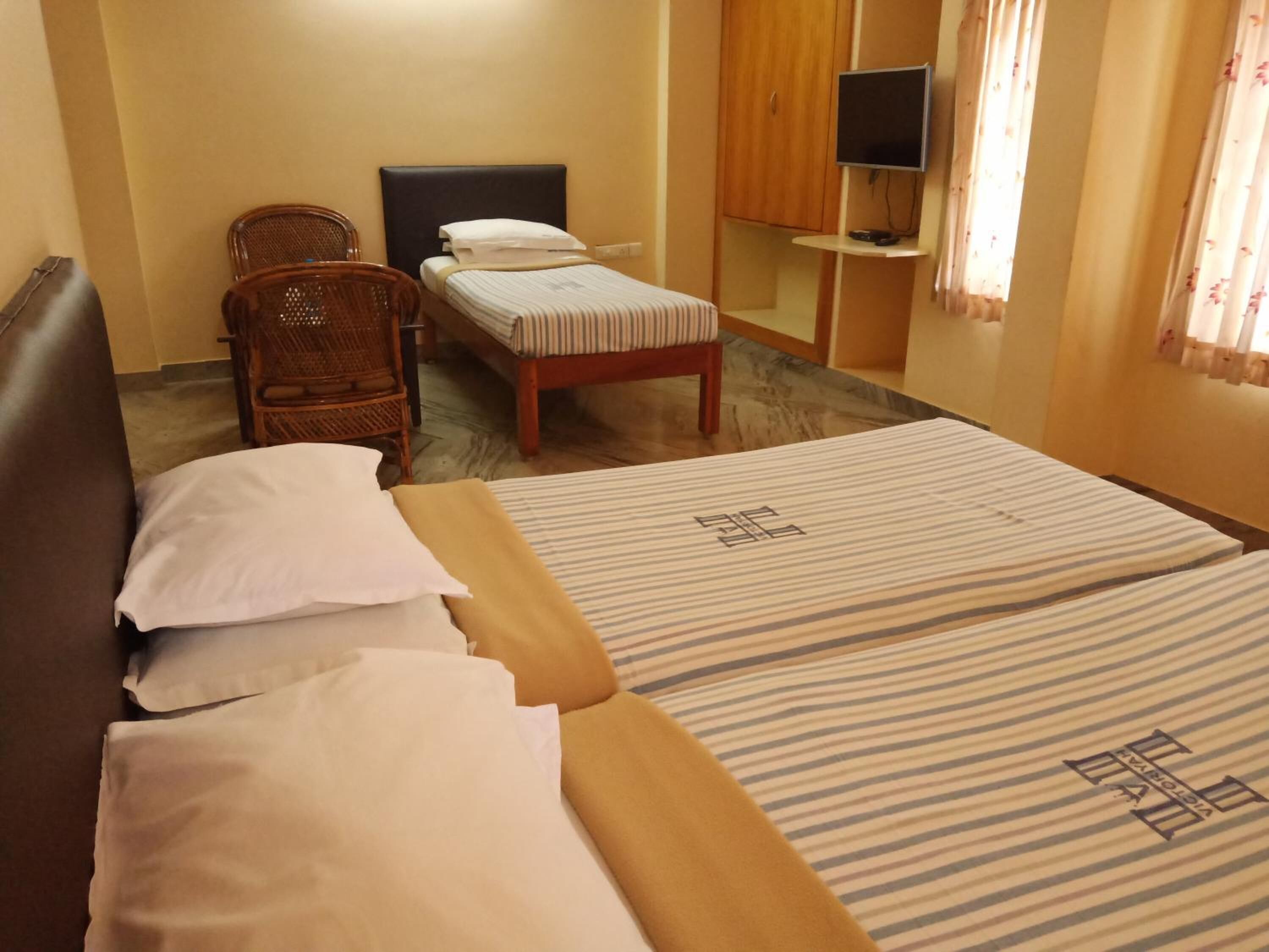 A hotel room with two single beds, a sofa, a chair, a TV, and a wardrobe.