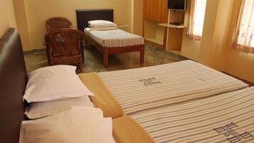 A hotel room with two single beds, a sofa, a chair, a TV, and a wardrobe.