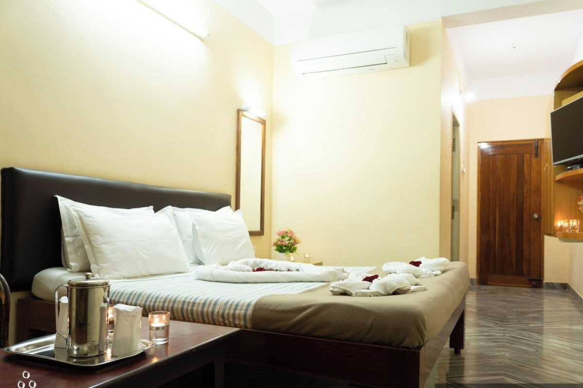 A hotel room with a bed, bedside table, TV, and a small table with a candle and a tray.