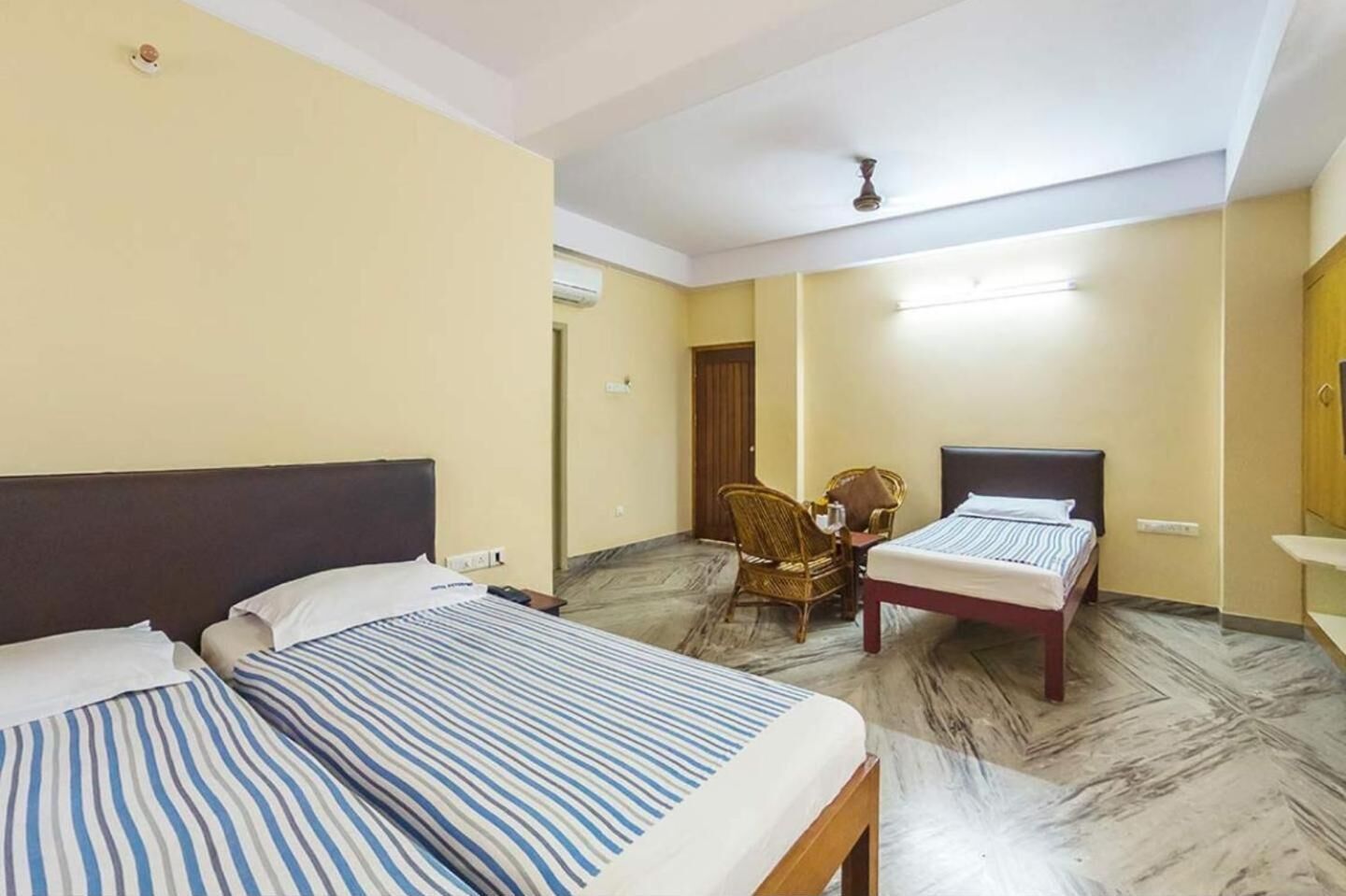 Habitación de hotel con dos camas, una silla, una mesita y un ventilador de techo.