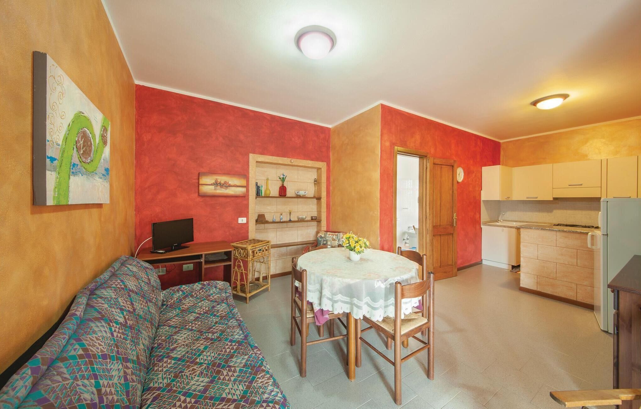 Ein Wohnzimmer mit einer Couch, einem Fernseher, einem Esstisch mit Stühlen und einer Küchenzeile mit Schränken und einem Kühlschrank.