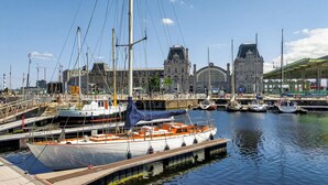 A marina with multiple boats docked, a large building with a distinctive architectural style in the background, and a clear blue sky. - Residentie De Kateie ref 15 (Ooostende)