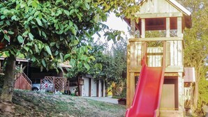 A wooden playhouse with a red slide, surrounded by trees and a house in the background. - 2 bedroom nice home in Schlitz-Rimbach (Schlitz-Rimbach)