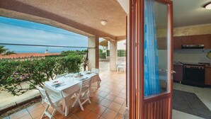 Ein Balkon mit Tisch für zwei Personen, Blick auf das Meer und einer Küchenzeile mit Herd.