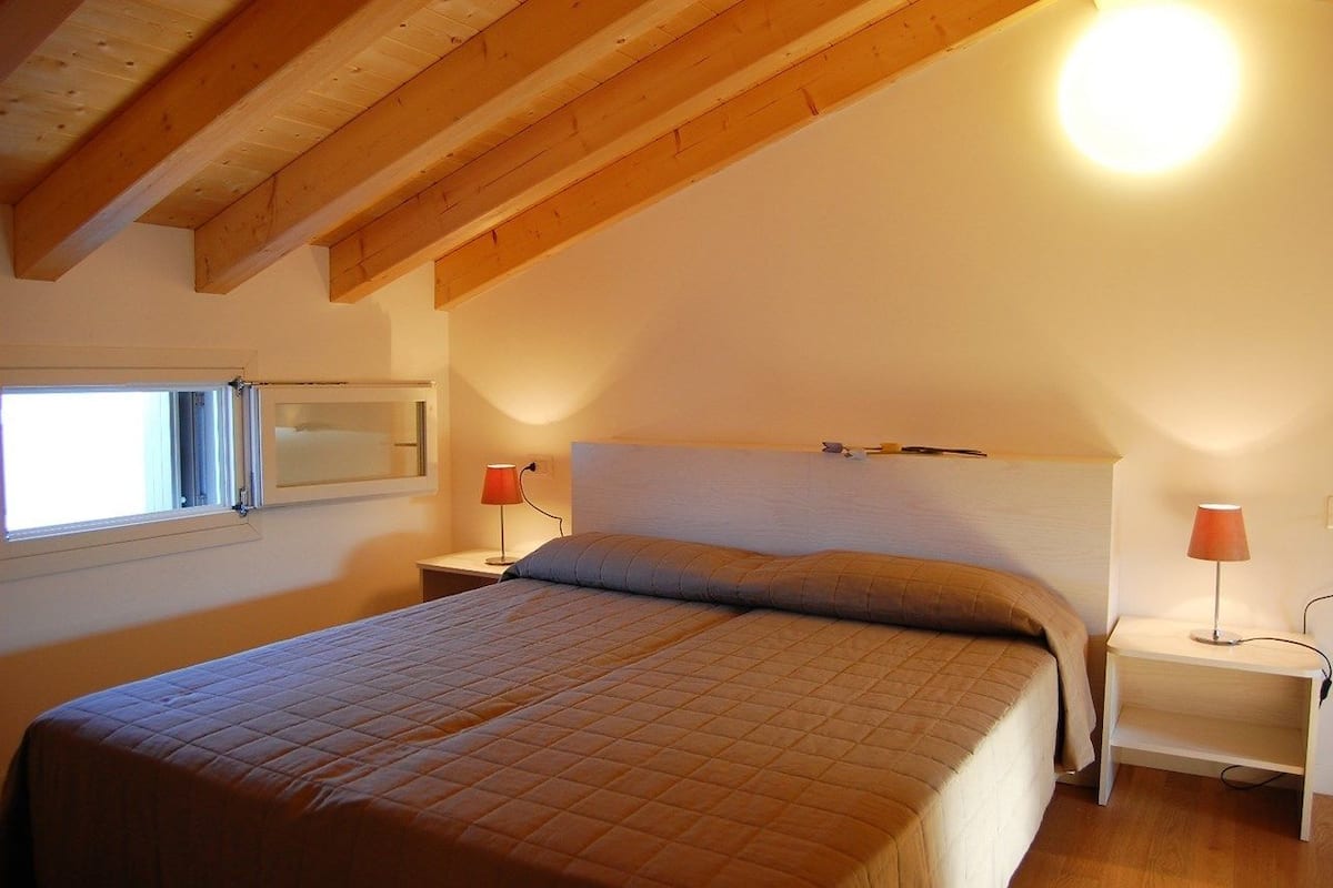 Ein Schlafzimmer mit einem Bett, zwei Nachttischen, einem Fenster und einer Deckenleuchte.