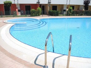 A swimming pool with a curved edge and a tiled deck. - Villaggio Leopardi (San Michele al Tagliamento)