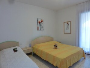 A hotel room with two single beds, a nightstand, a bedside table, and a window with curtains. - Villaggio Leopardi (San Michele al Tagliamento)