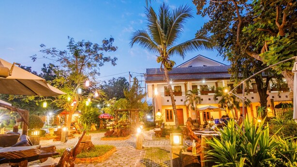A well-lit outdoor area with wooden furniture, a cobblestone path, and a building with a tiled roof. - Huandalha Resort Lumphun (Lamphun)