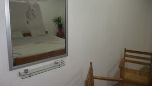 A bedroom with a bed, a bedside table, a chair, a mirror, and a potted plant. - Sigiri Lodge (Sigiriya)