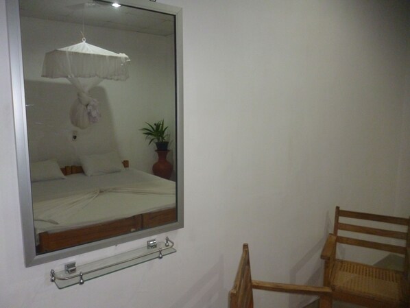 A bedroom with a bed, a bedside table, a chair, a mirror, and a potted plant.