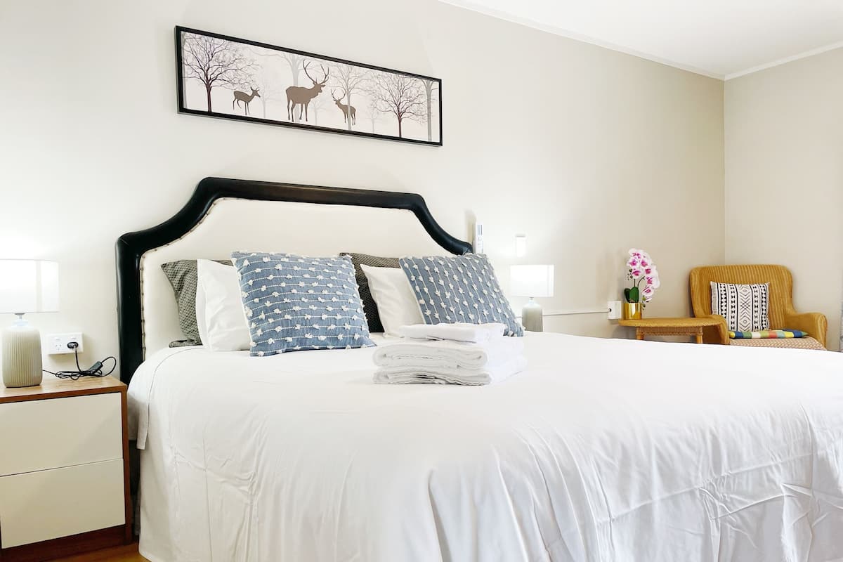 A neatly made bed with a white comforter and blue patterned pillows, a bedside table with a lamp, and a framed deer artwork on the wall.