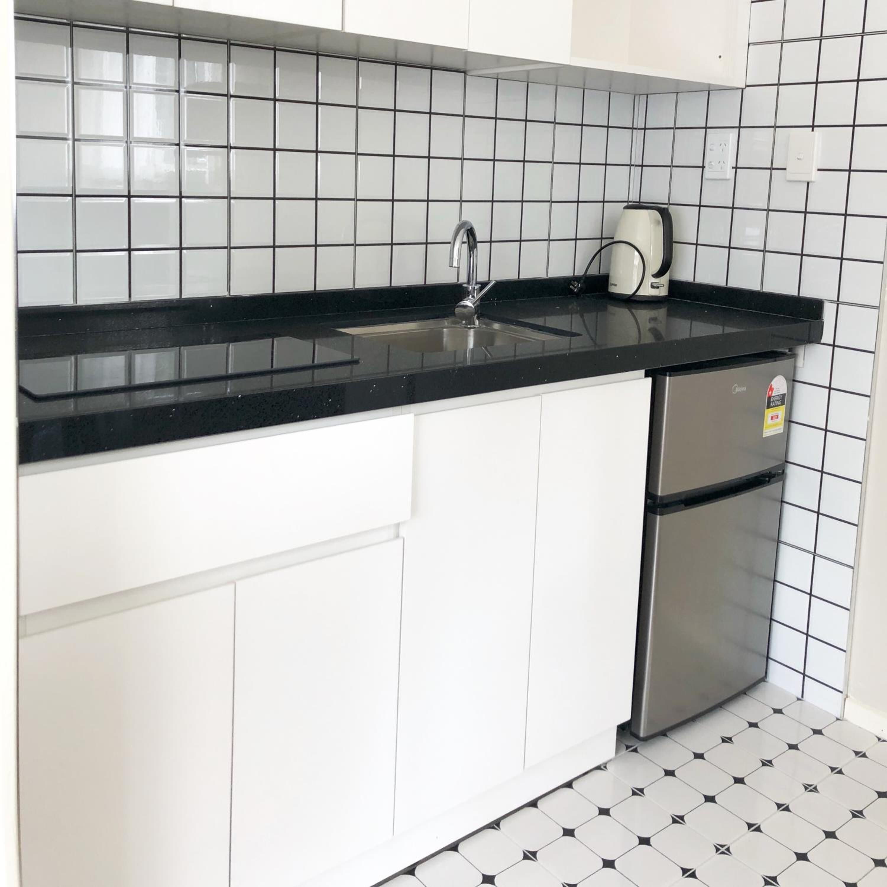 Cozinha com bancada preta, eletrodomésticos de aço inoxidável e armários brancos.