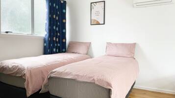 Un dormitorio con dos camas, una ventana con cortinas, aire acondicionado montado en la pared y una cita enmarcada en la pared.