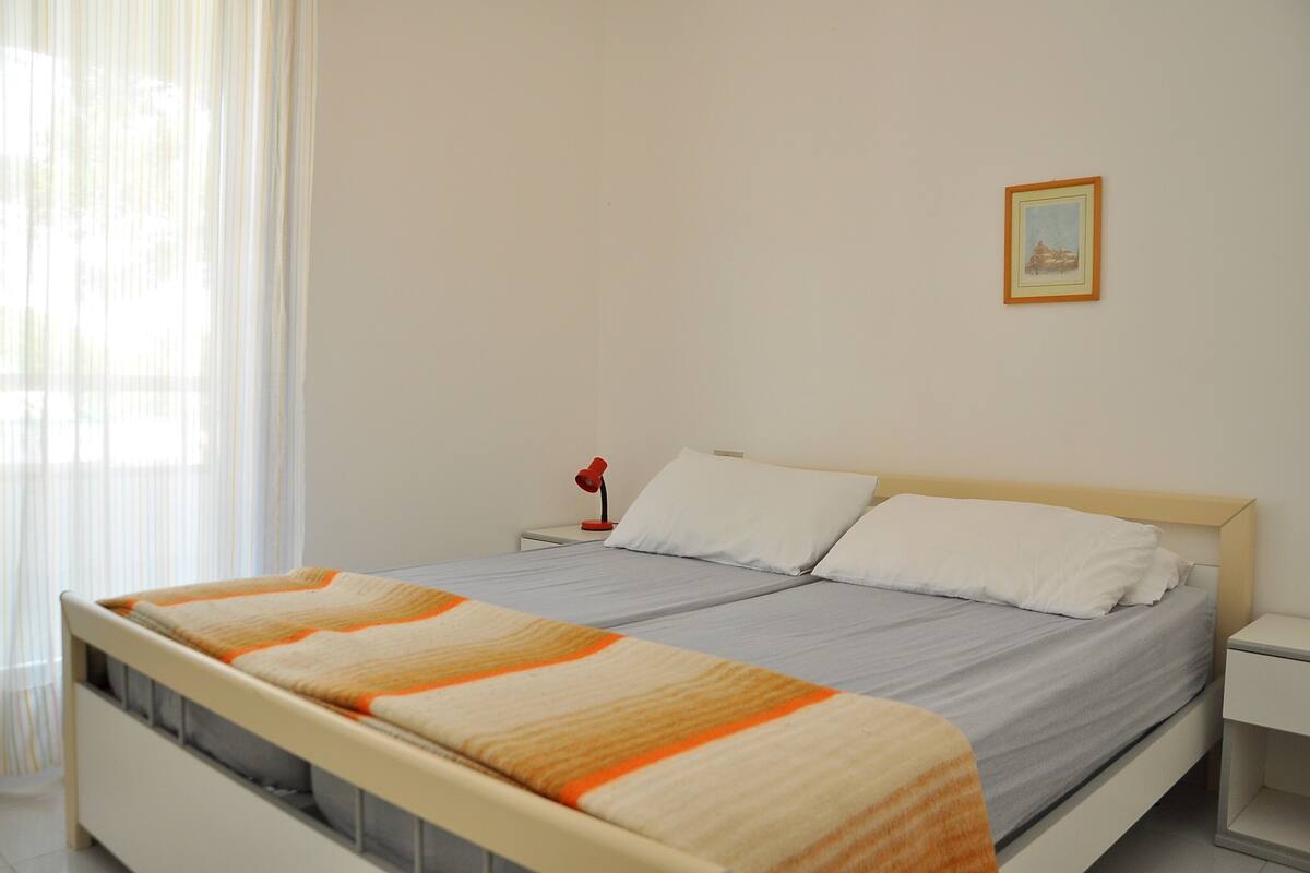 A neatly made bed with a striped blanket, a bedside lamp, and a framed picture on the wall.