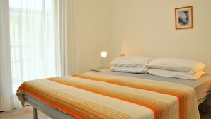 A neatly made bed with a striped blanket, a bedside lamp, and a framed picture on the wall. - Condominio Tucano (San Michele al Tagliamento)