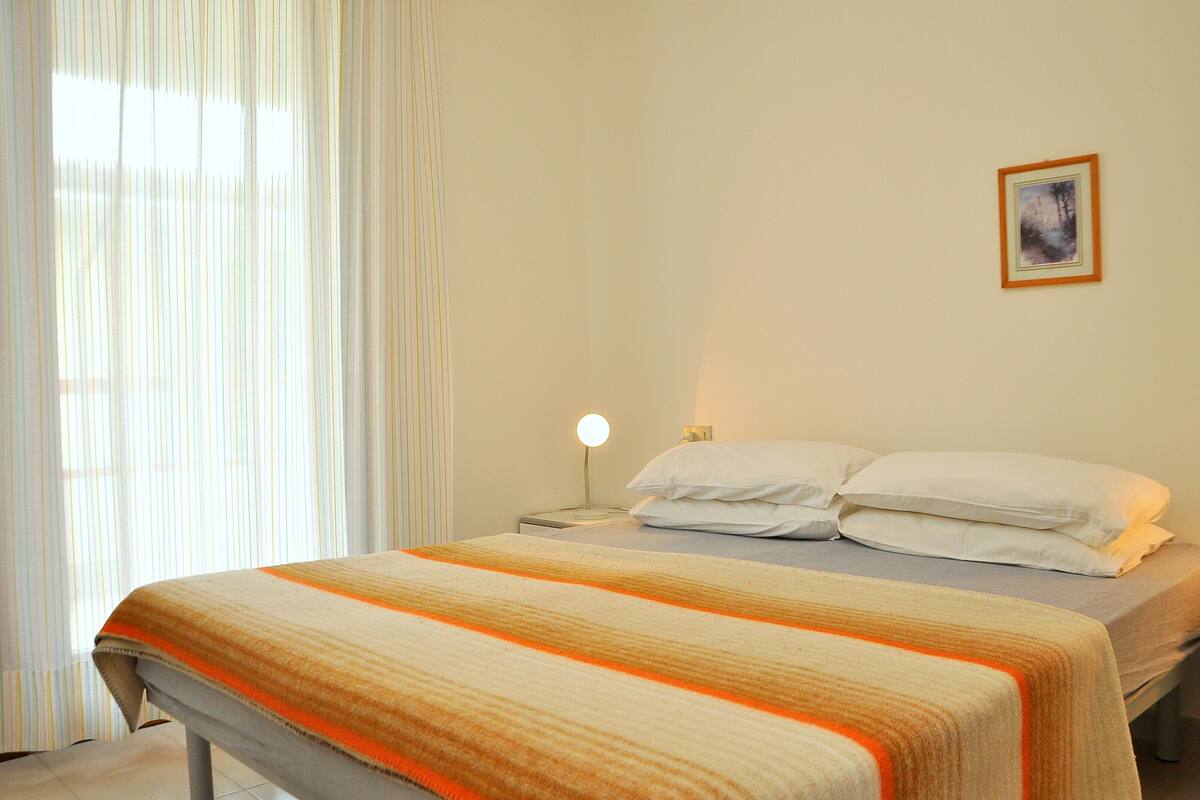 A neatly made bed with a striped blanket, a bedside lamp, and a framed picture on the wall.
