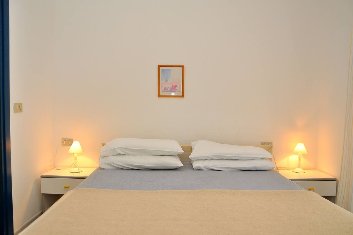 A neatly made bed with two pillows and a bedside lamp on each side.