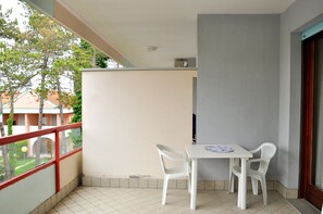 A balcony with a white table and two white chairs, a red railing, and a view of trees and buildings.