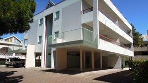 A multi-story building with balconies, a parking area, and a clear sky. - Condominio Tucano (San Michele al Tagliamento)