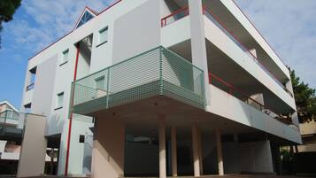 Ein mehrstöckiges Gebäude mit flachem Dach, einem grünen Metallbalkon im zweiten Obergeschoss und einem roten Geländer.