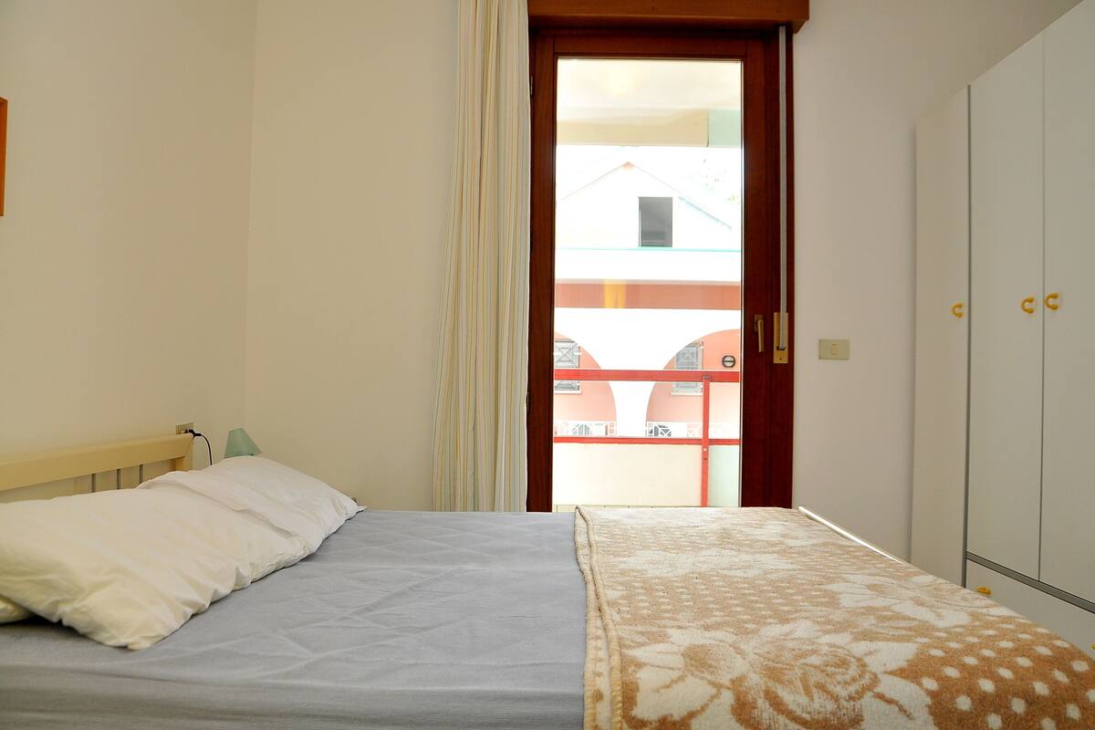 A bedroom with two beds, a wardrobe, and a view of a building through a door.