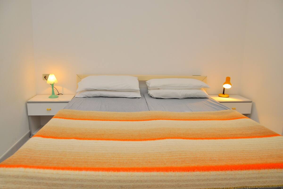A bed with a striped blanket, two pillows, and two bedside lamps.