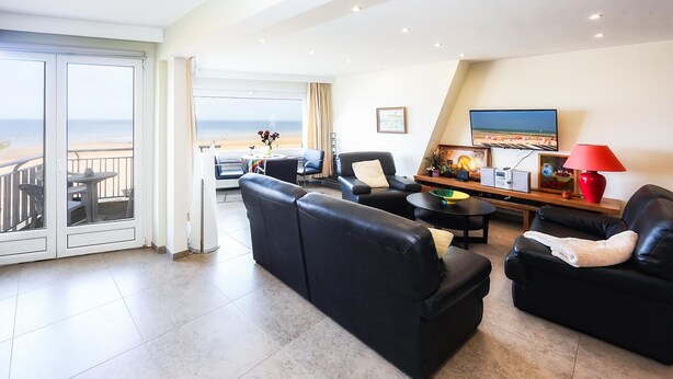 A living area with a sofa, armchairs, a coffee table, and a TV. There is a balcony with a view of the beach. - Costa Brava 3e Ref. Nr 202 (Oostende)
