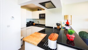 A modern kitchen with a black countertop, white cabinets, a microwave, a coffee maker, and a red lamp. - Costa Brava 3e Ref. Nr 202 (Oostende)