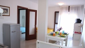 A compact hotel room with a kitchenette, a dining area, and a bathroom visible through an open door. - Residence Gemini (San Michele al Tagliamento)