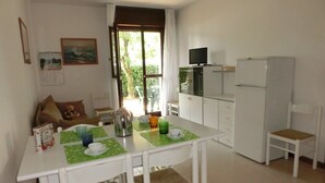 A compact kitchen with a dining table, chairs, and a refrigerator. - Residence Gemini (San Michele al Tagliamento)