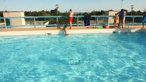 A swimming pool with clear blue water, a tiled deck, and a metal railing. - Residence Gemini (San Michele al Tagliamento)