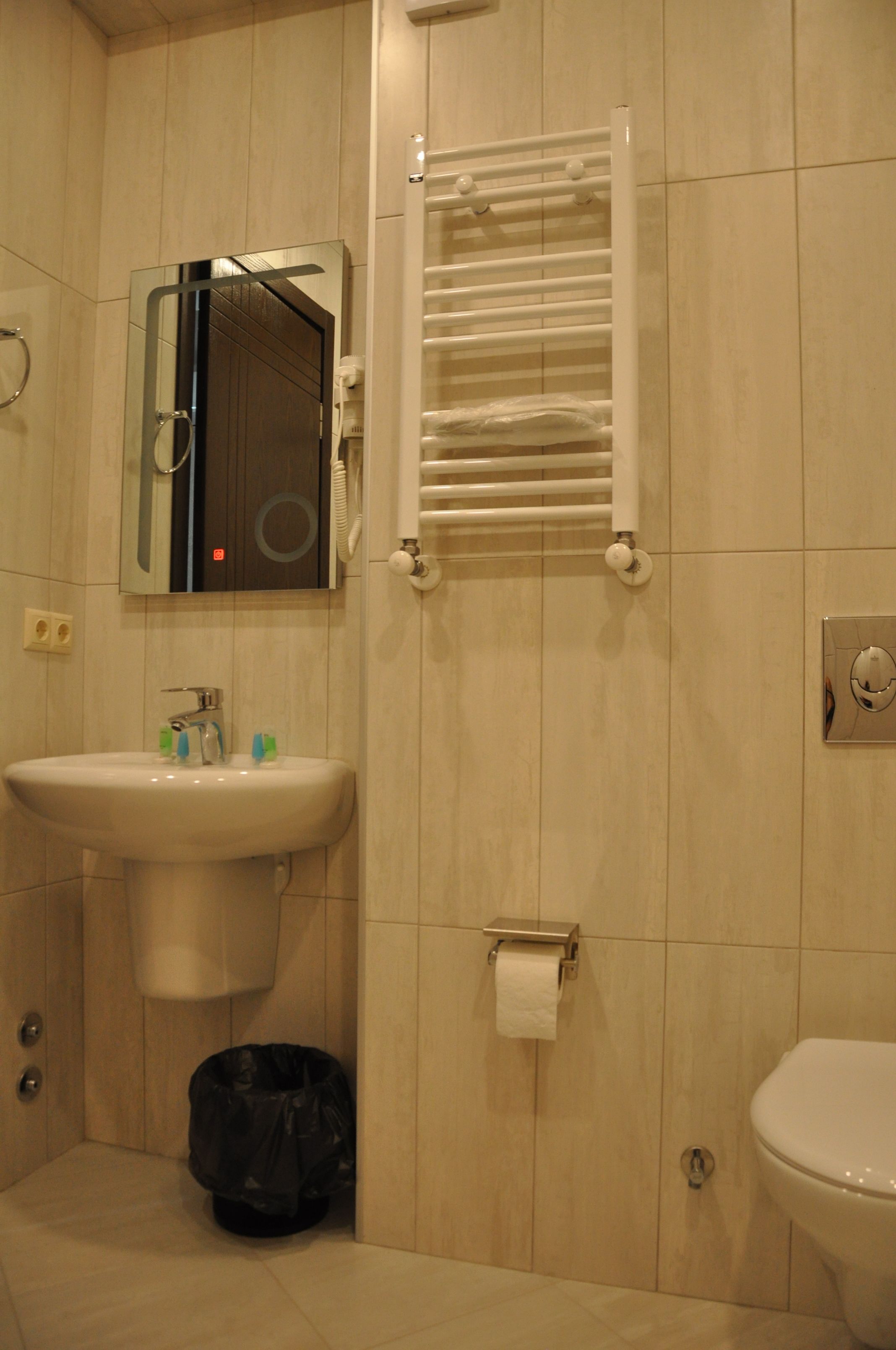 A bathroom with a sink, mirror, towel rack, toilet, and a trash bin.