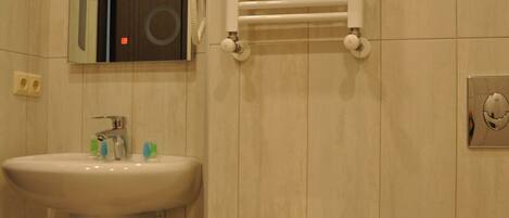 A bathroom with a sink, mirror, towel rack, toilet, and a trash bin.
