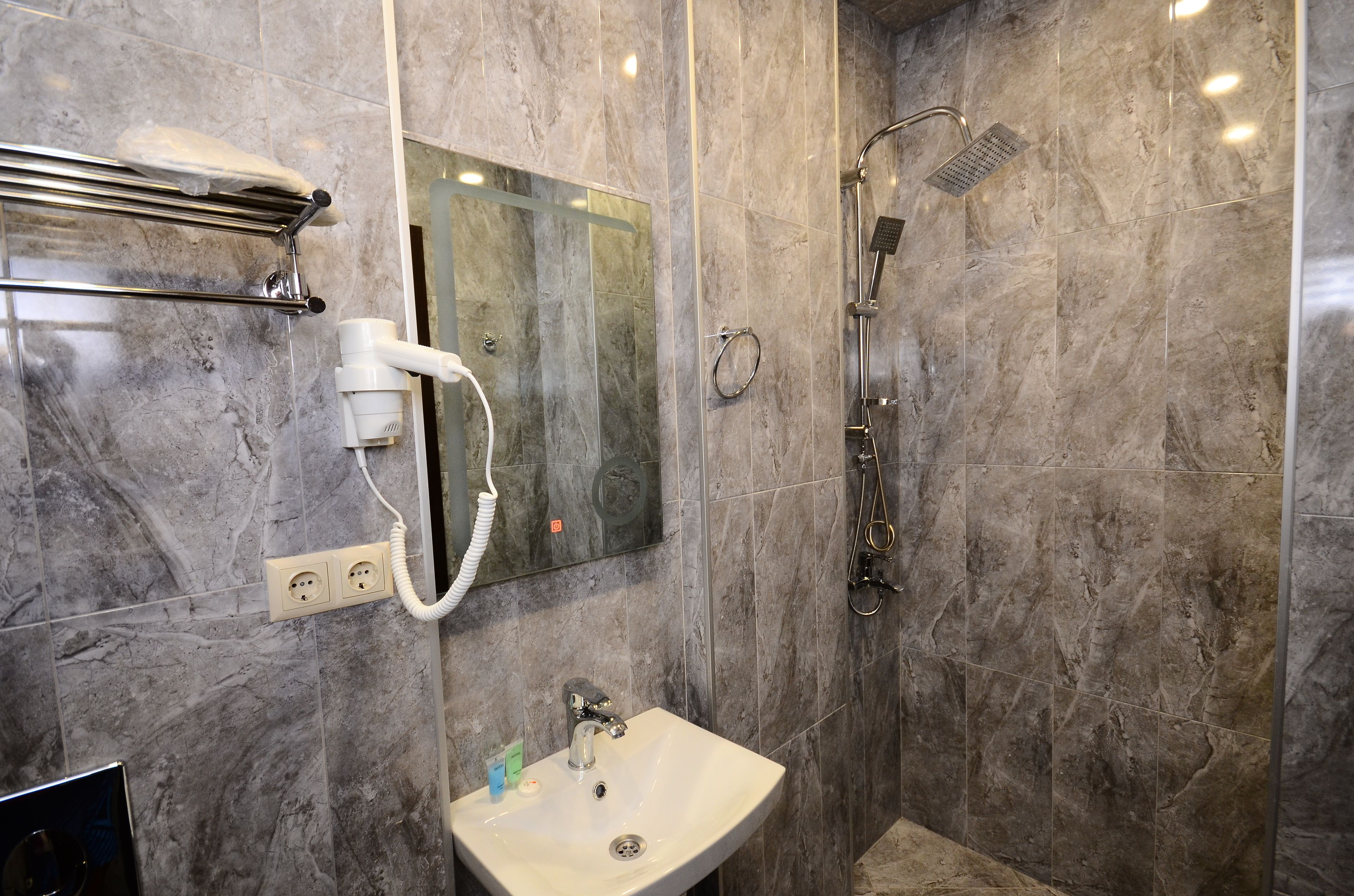 A modern bathroom with a marble wall, a sink, a towel rack, and a shower with a handheld showerhead.