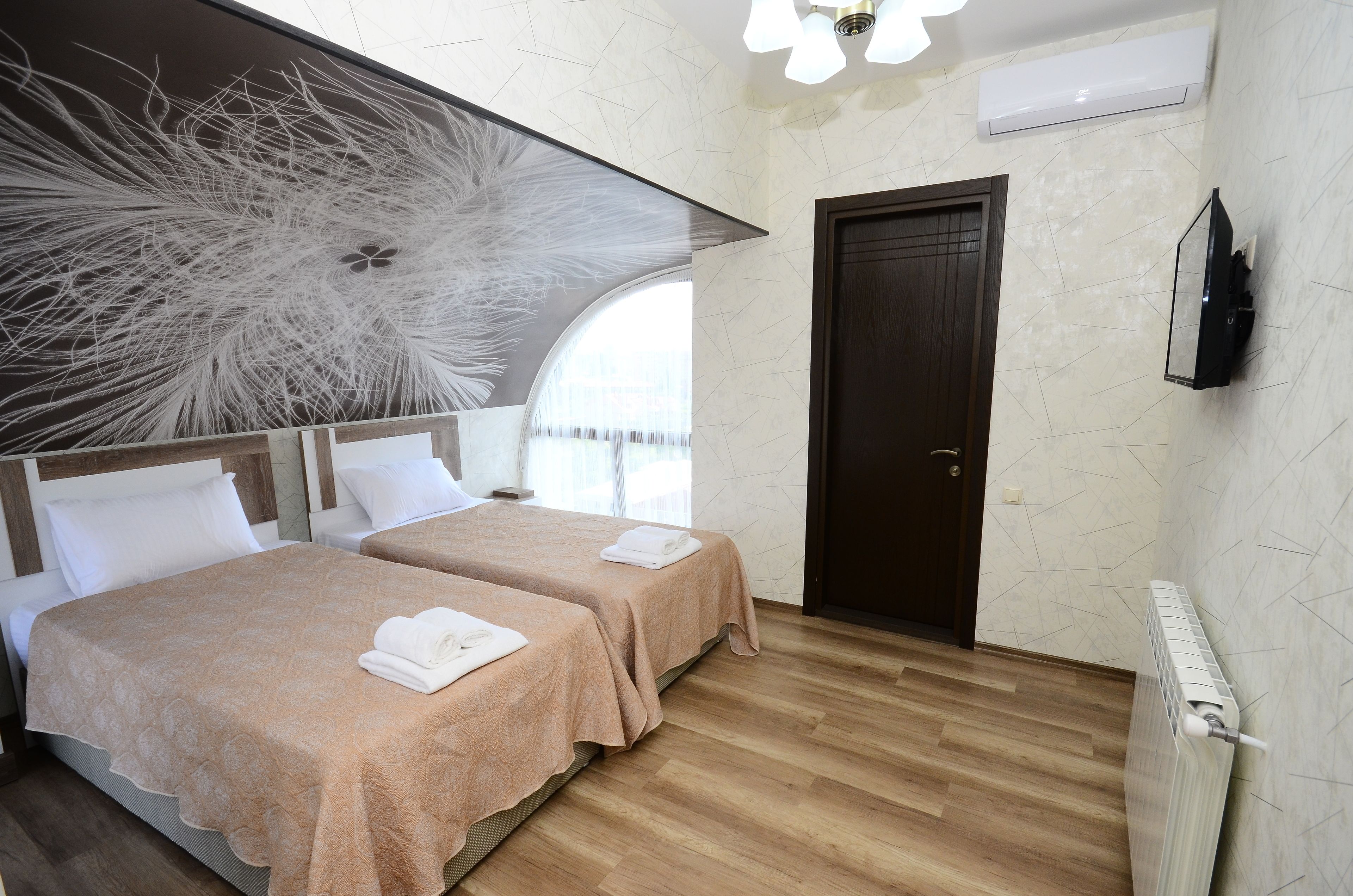 A hotel room with two beds, a large abstract artwork on the wall, a wooden floor, a dark door, and a mounted TV.