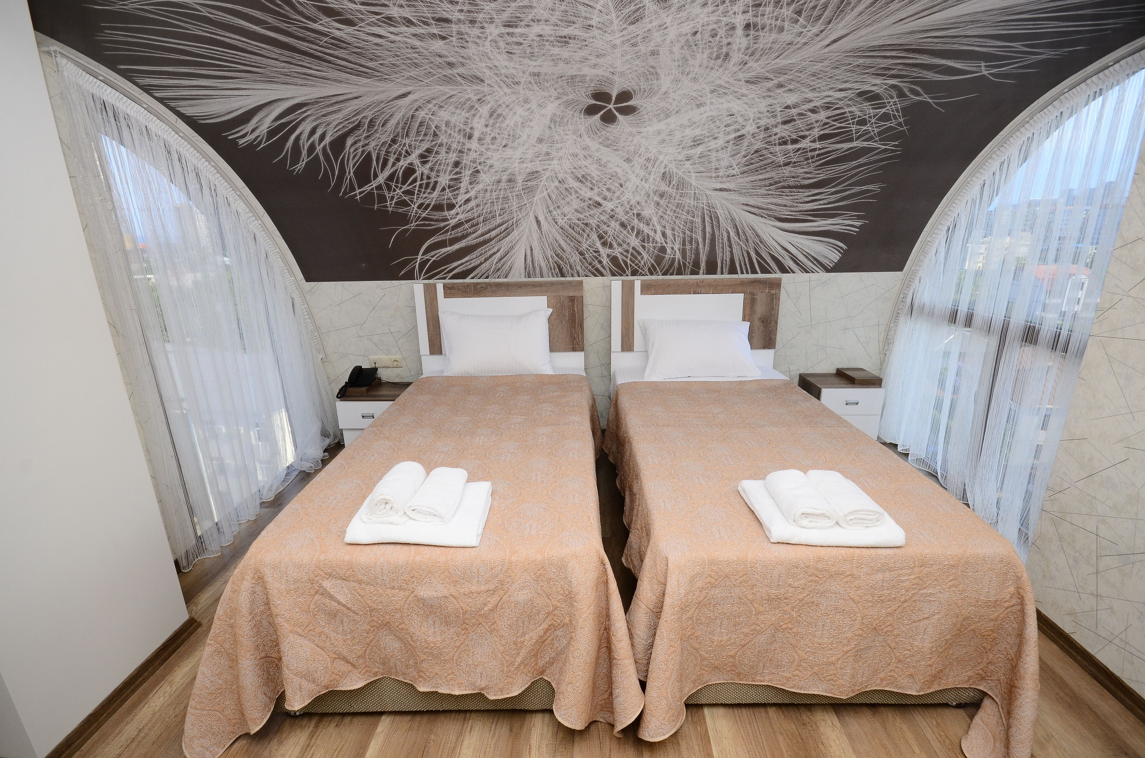 Ein Hotelzimmer mit zwei Betten, jeweils mit einer rosafarbenen Tagesdecke und weißen Handtüchern. Das Zimmer zeichnet sich durch ein außergewöhnliches Decken-Design mit einem großen, abstrakten Muster aus.