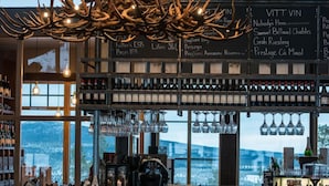 A bar area with a high ceiling, a large chandelier, and a view of the mountains through the windows. - Mountain Lodge (Salen)
