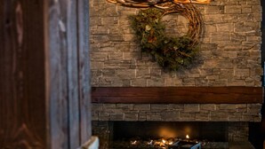 A stone fireplace with a deer antler chandelier, a lit candle, and a small table with a board game. - Mountain Lodge (Salen)
