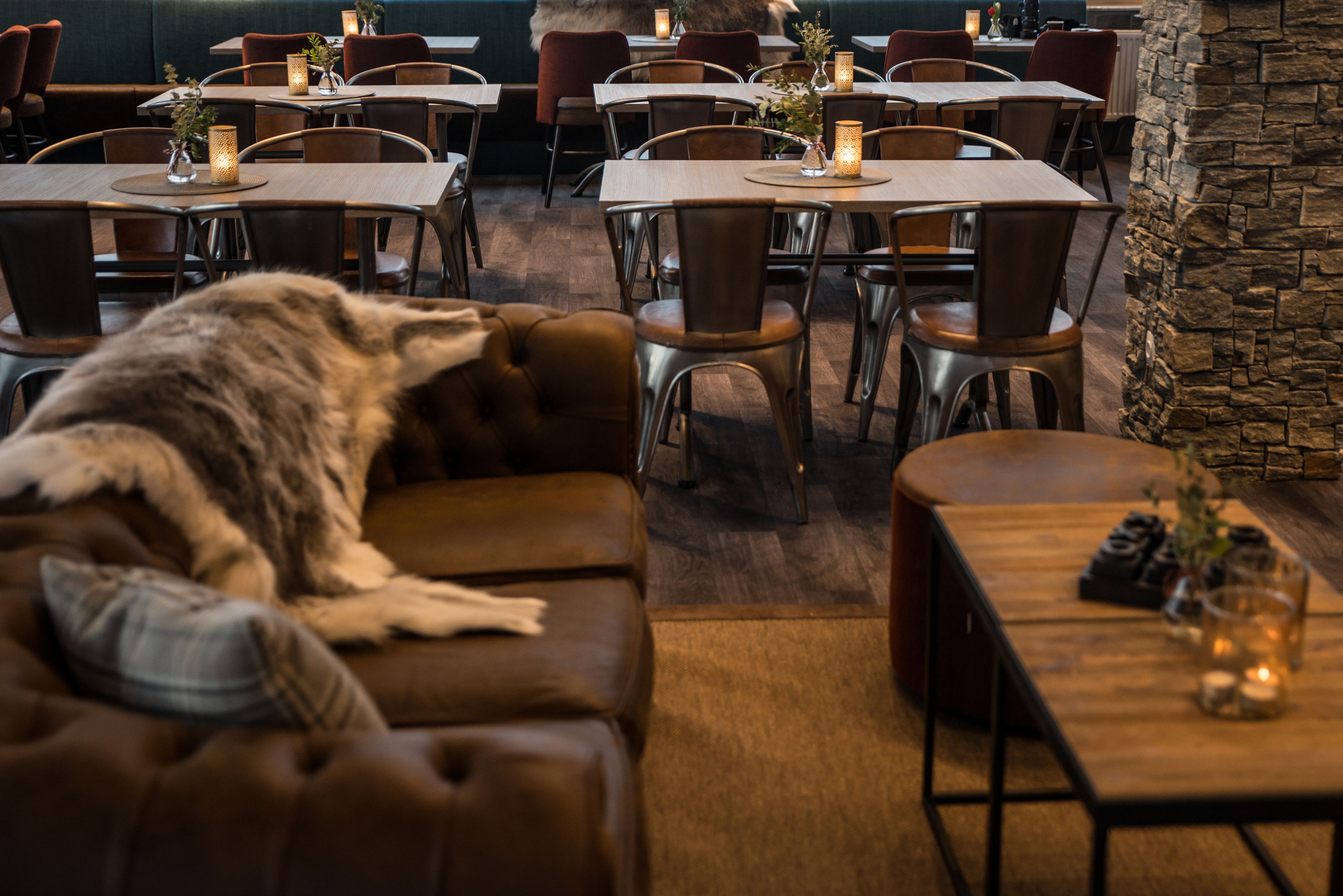 Een restaurant met meerdere tafels en stoelen, een stenen muur en een hond die op een bank ligt.