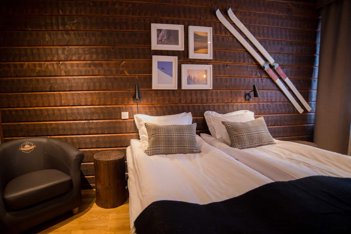 A wooden cabin room with two beds, a chair, and a ski rack.