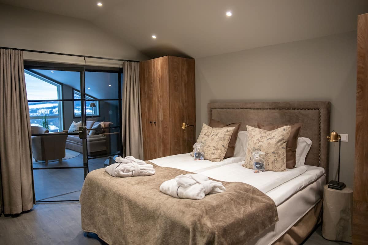 A modern hotel bedroom with a large bed, a wooden wardrobe, and a balcony with a view.