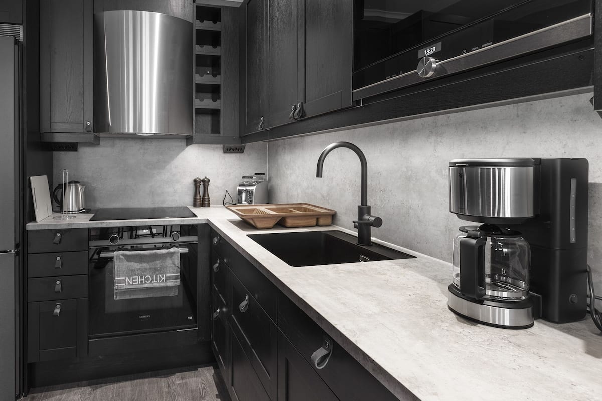 A modern kitchen with a stainless steel range hood, a built-in oven with a kitchen towel, a sink with a faucet, and a coffee maker.