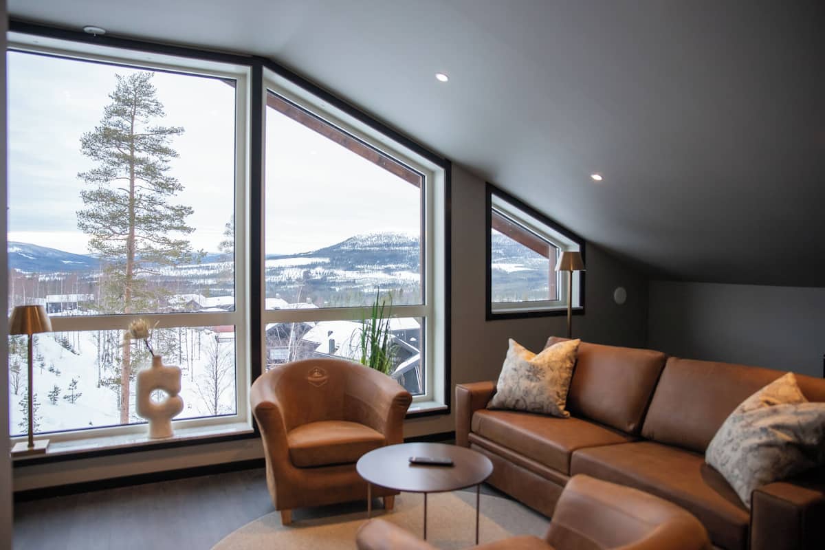 A modern living room with a large window offering a view of a snowy landscape and a mountain.