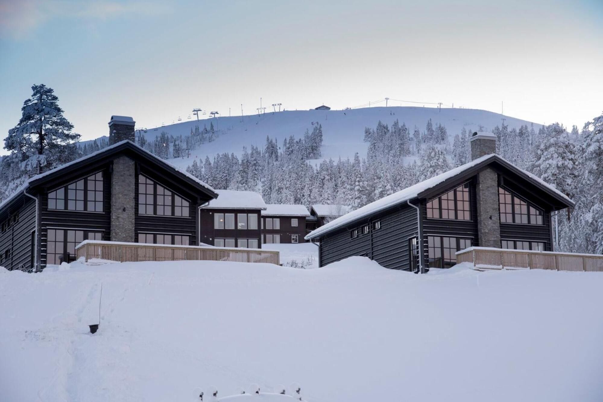 A snow-covered lodge with multiple log cabins, a ski slope in the background, and a forested mountain.