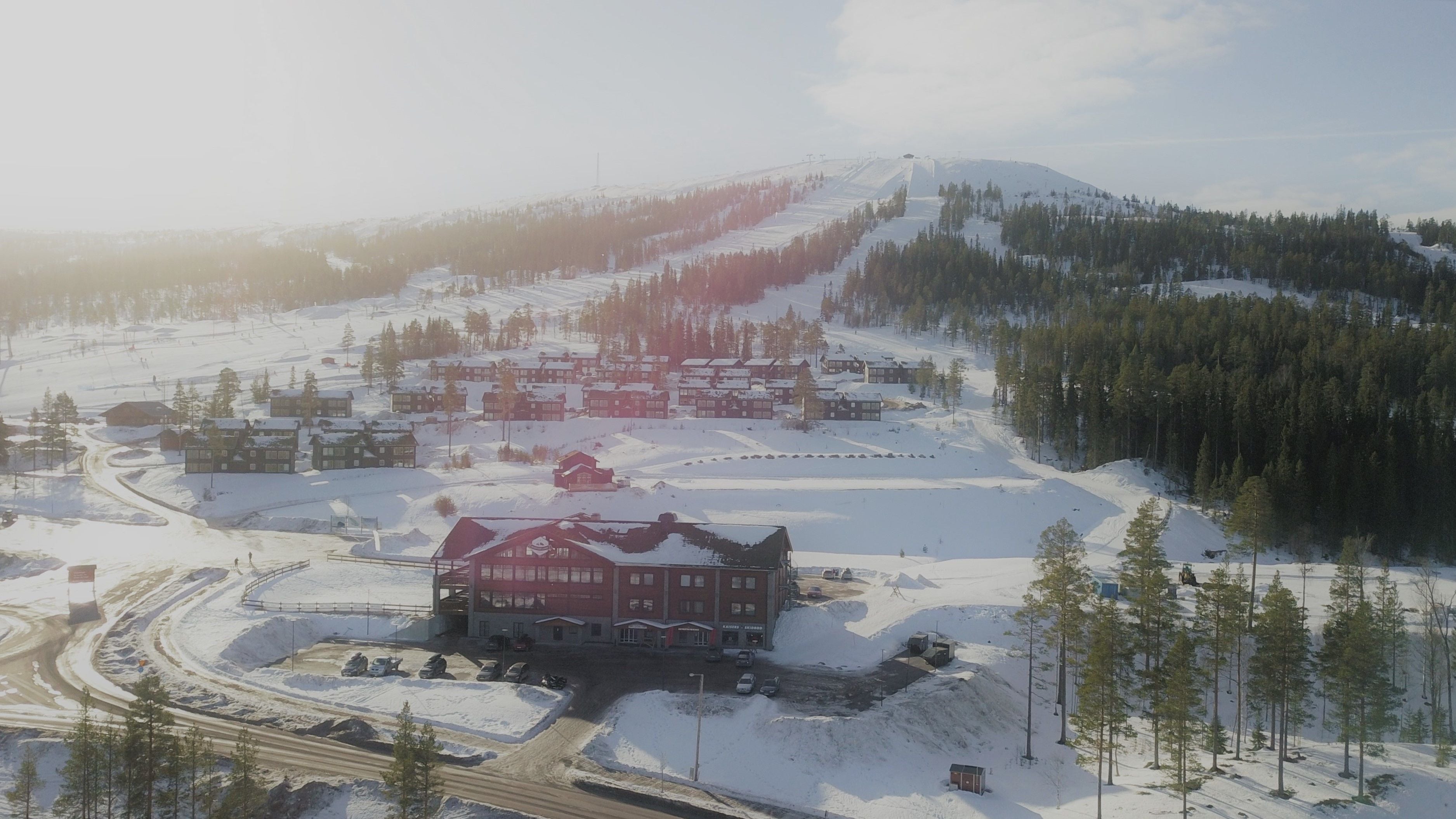 Une ville de montagne enneigée, avec un imposant bâtiment rouge au centre, entourée de routes et de maisons recouvertes de neige.