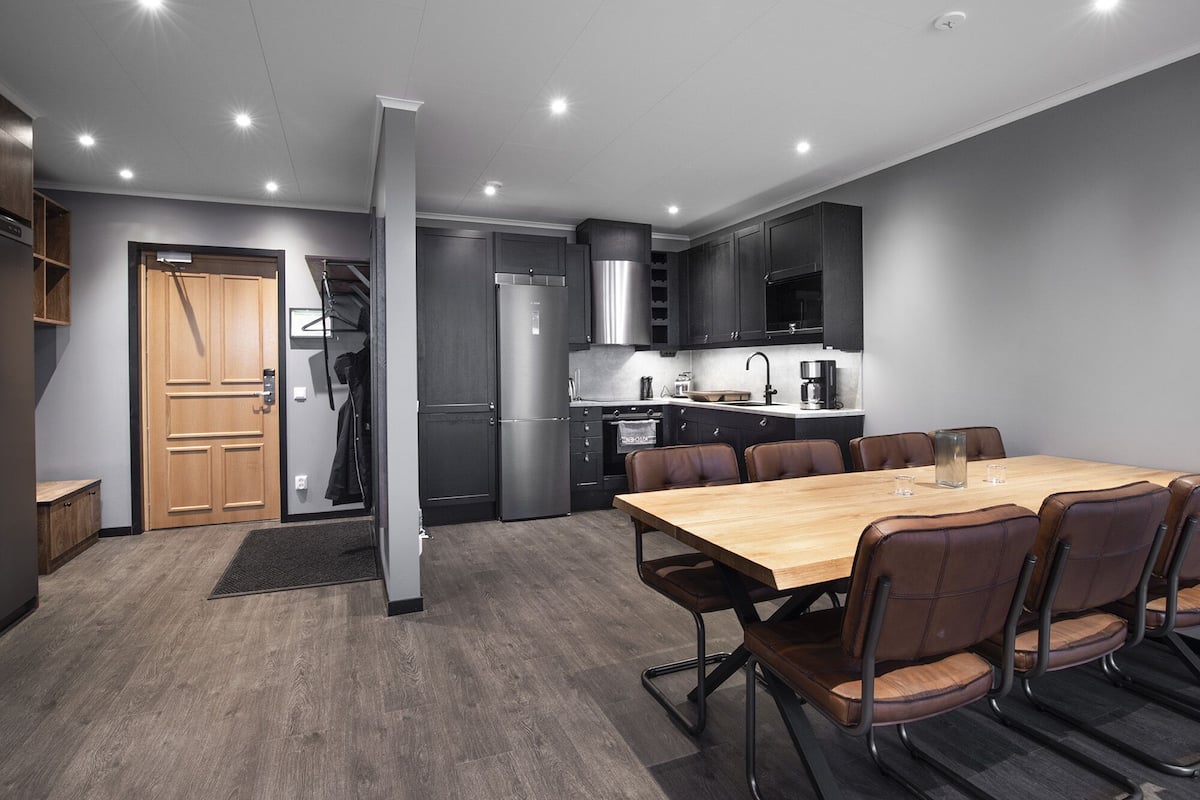 A modern kitchen with dark cabinetry, stainless steel appliances, and a wooden dining table with leather chairs.