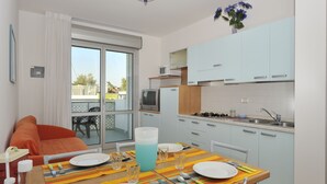 Una cocina moderna con armarios blancos, un comedor con una mesa para dos personas y un sofá en la zona de estar contigua.