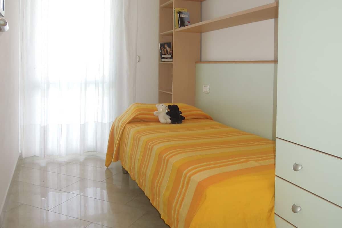 Una stanza con un letto, un armadio, una scaffalatura e una finestra con tende.