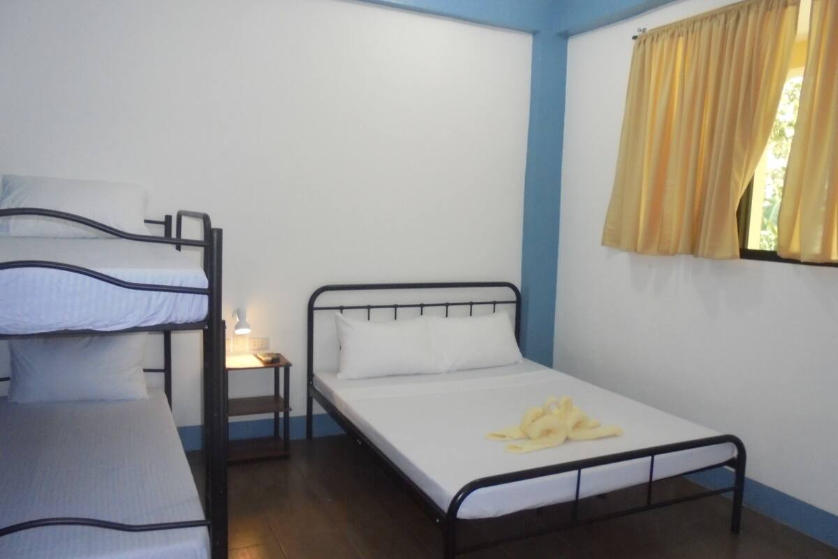A room with a bunk bed, a single bed, a nightstand with a lamp, and a window with curtains.