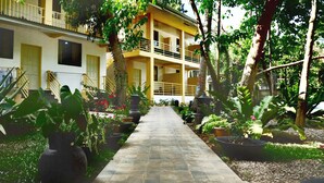 A pathway leading to a building with multiple balconies, surrounded by lush greenery and potted plants. - Maya Playa (Panglao)